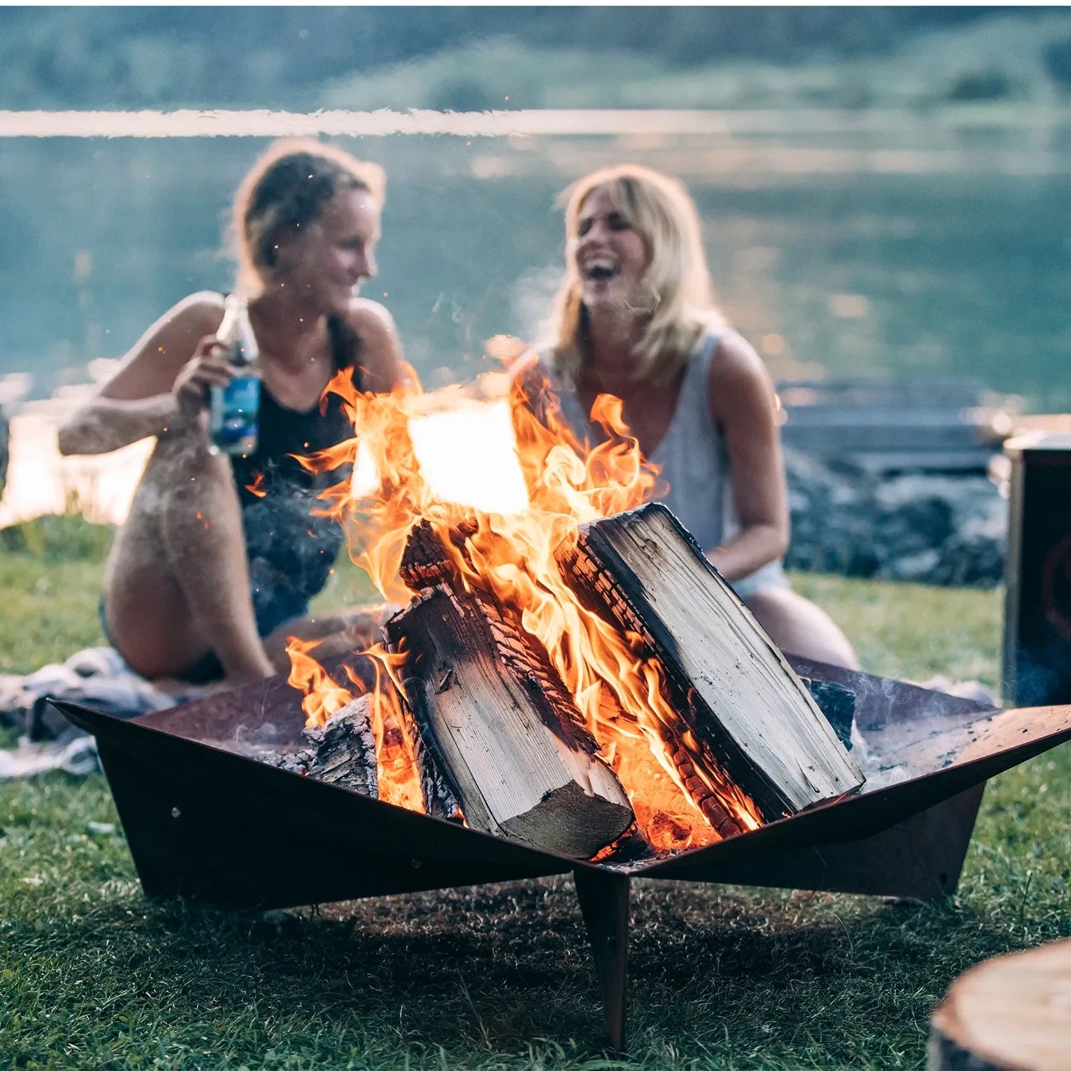 Höfats TRIPLE 120 Fire Pit in Corten Steel with burning logs, placed on a white surface.